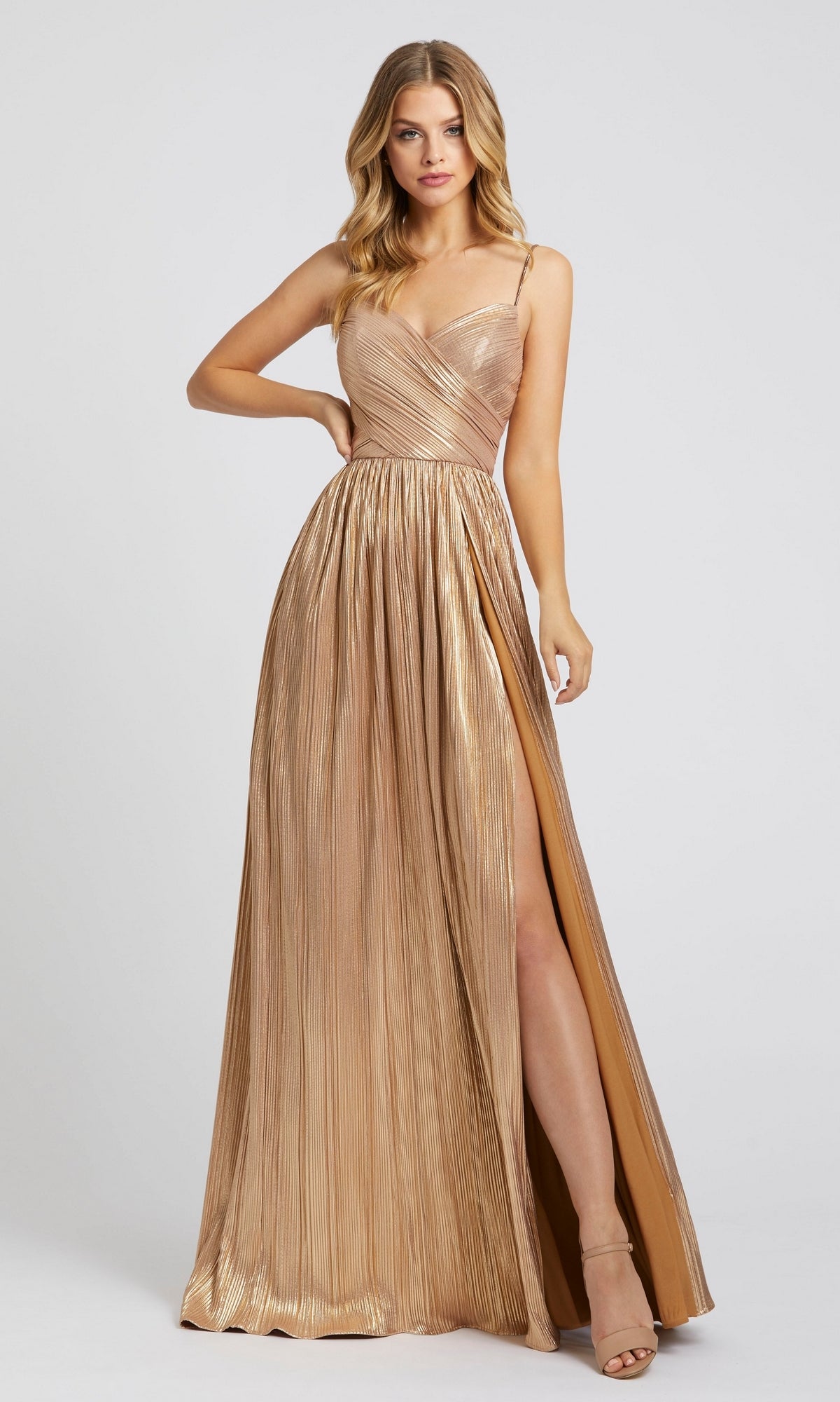 A woman models the Mac Duggal 26275, a long gold pleated formal dress with spaghetti straps and a high slit, posing against a plain light background.